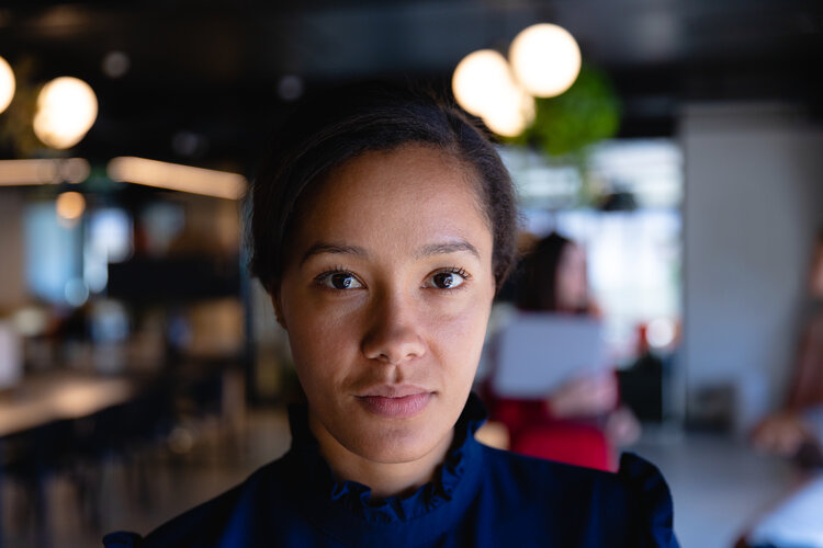 Portrait of a mixed race businesswoman wearing navy blue smart clothes, working in modern office, looking straight into a camera.